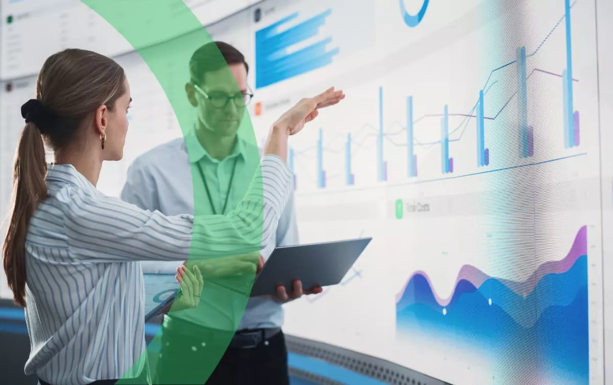 Woman and man actively chatting in front of big screen and showing graphs